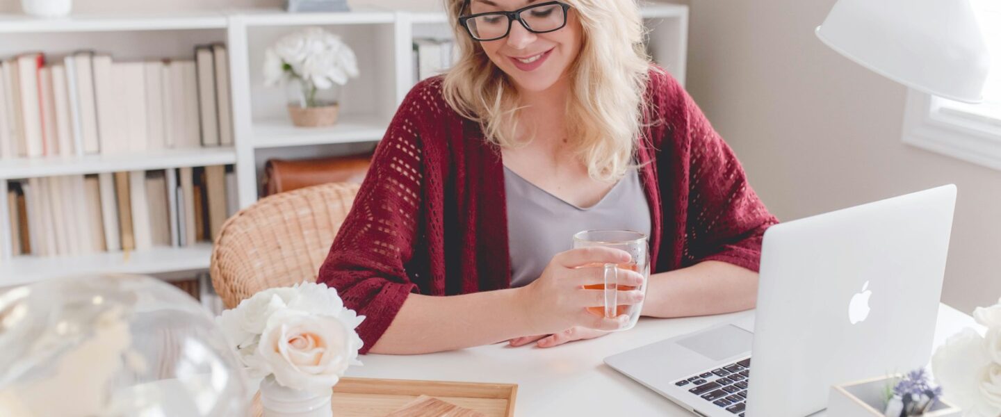 woman smiling holding glass mug sitting beside table with MacBook